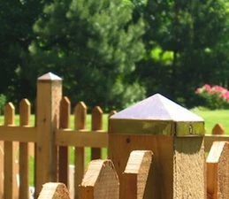 New copper pyramid post cap, bright, on a wood picket fence post