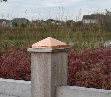 Copper pyramid post cap warming toward bronze on a wood fence post