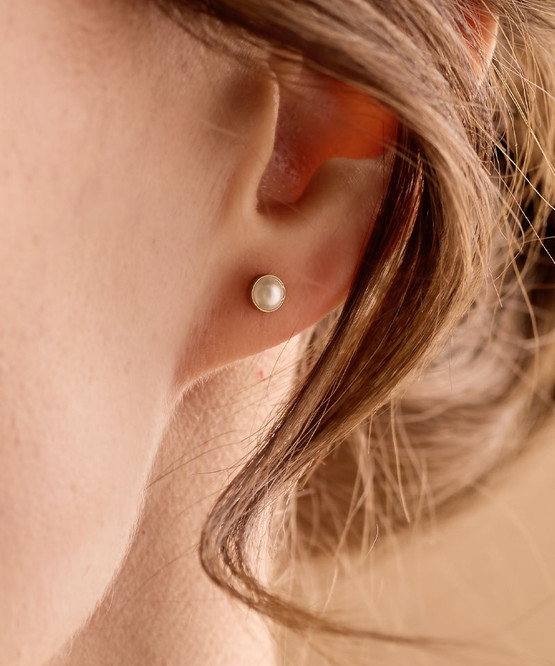 Up close image of model wearing the Nickel-Free Golden Titanium 5mm Bezel White Pearl Earrings