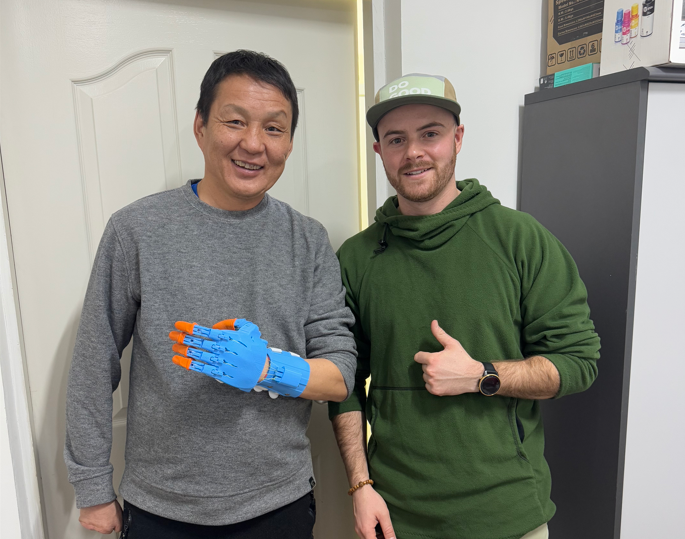 A man with a prosthetic hand and the technician who created it standing side by side