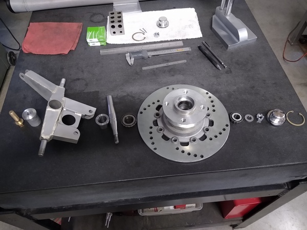 Wheel hub and suspension components arranged in sequence on a table beside the upright.
