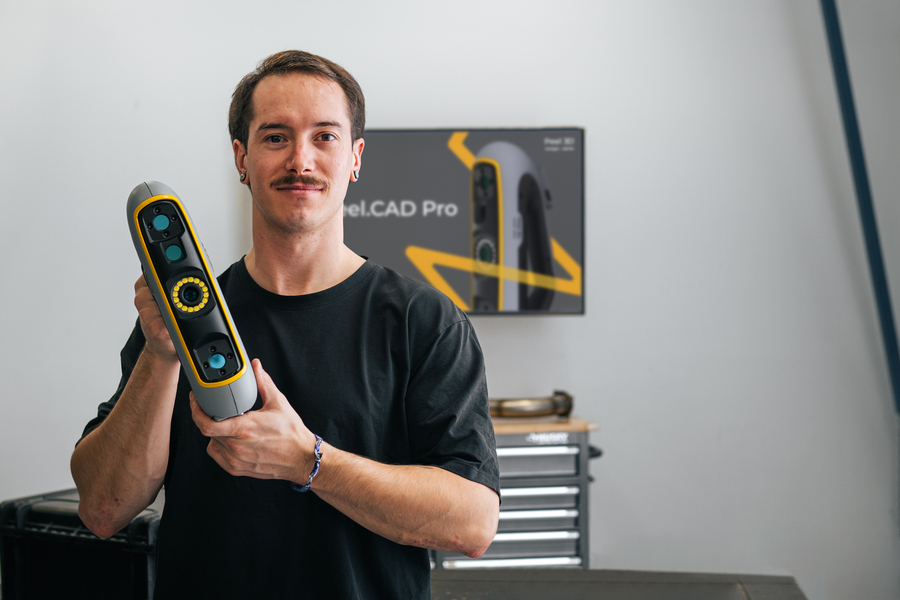 Technician in a workshop facing the camera and holding a Peel 3 scanner in his hands with Peel.CAD Pro displayed on a screen in the background.