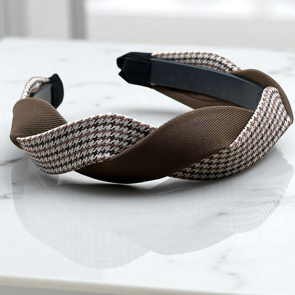 Side view of brown and white houndstooth fabric headband with a twisted top design. Side view of brown and white houndstooth fabric headband with a twisted top design.
