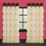 This window treatment features cascading cream-colored drapery panels elegantly hung from black seashell medallions, creating a layered and luxurious look. The bold pink walls, distressed black-hued flooring, and black window frame provide a dramatic contrast that highlights the soft, flowing fabric.