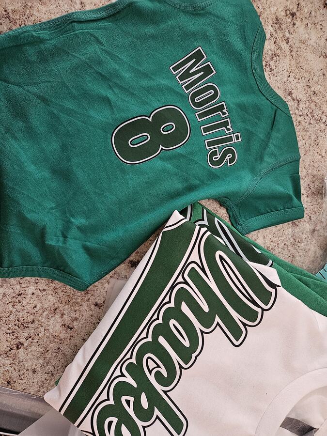 Green personalized shirt with the name Morris and number 8 beside a white shirt with green script lettering.