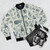 Pastel bomber jacket with a mythical creature pattern, including designs like Nessie, Bigfoot, and dragons. - Flat lay