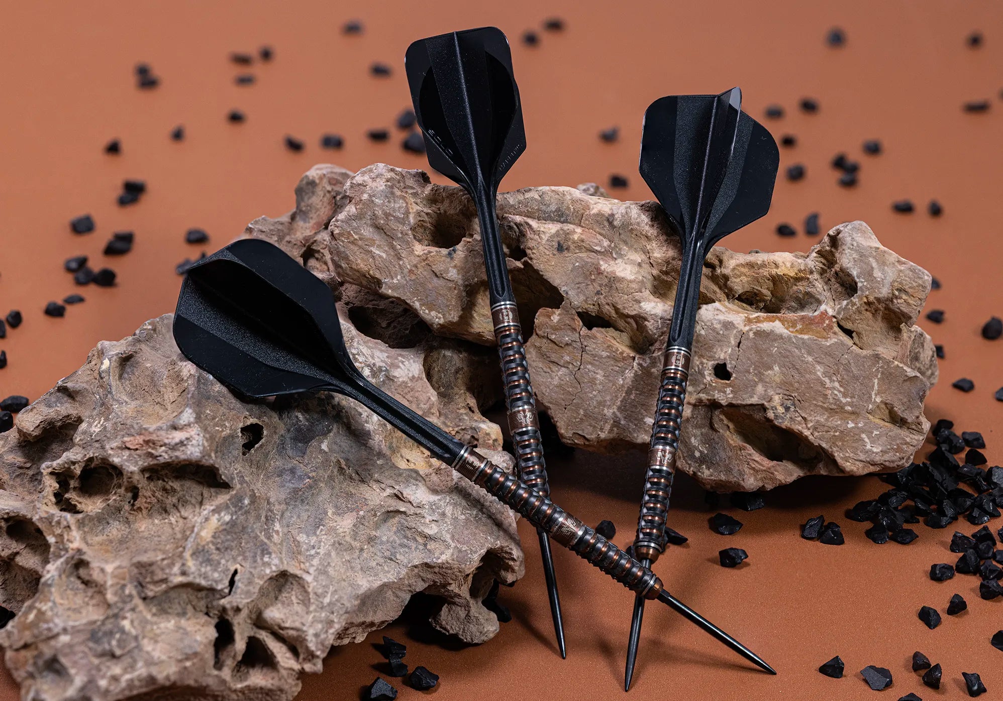 Harrows Wolfram Trinity darts with detailed copper-toned barrels and black flights, photographed against warm stone