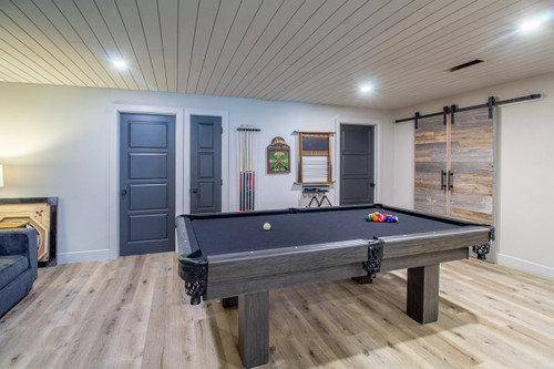Canada Billiard Invitation pool table with grey wood finish, black basket pockets and dark cloth in a recreation room.