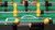 Close-up of foosball table with yellow and black players, ball near goal and metal rods in play.