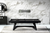 Modern black pool table with sleek angular legs in a stylish room featuring a marble accent wall, contemporary chandelier, and decorative sideboard with mirror.