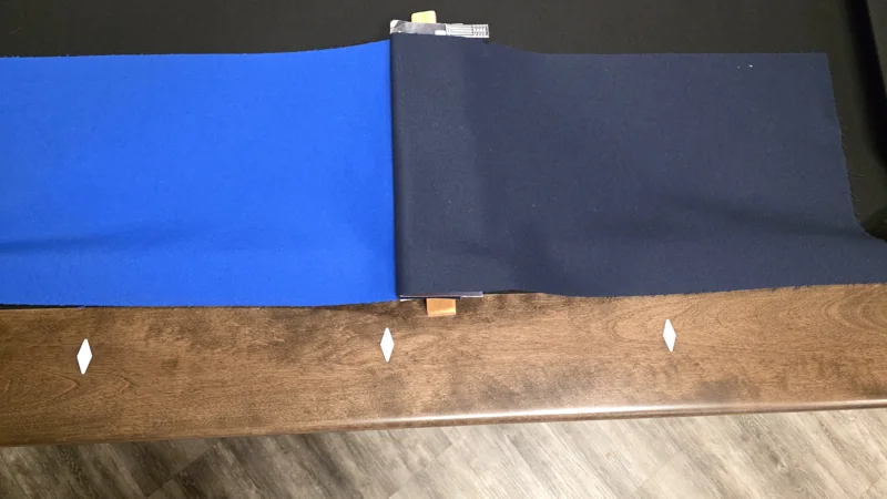 Blue and navy cloth samples compared against a timber pool-table rail