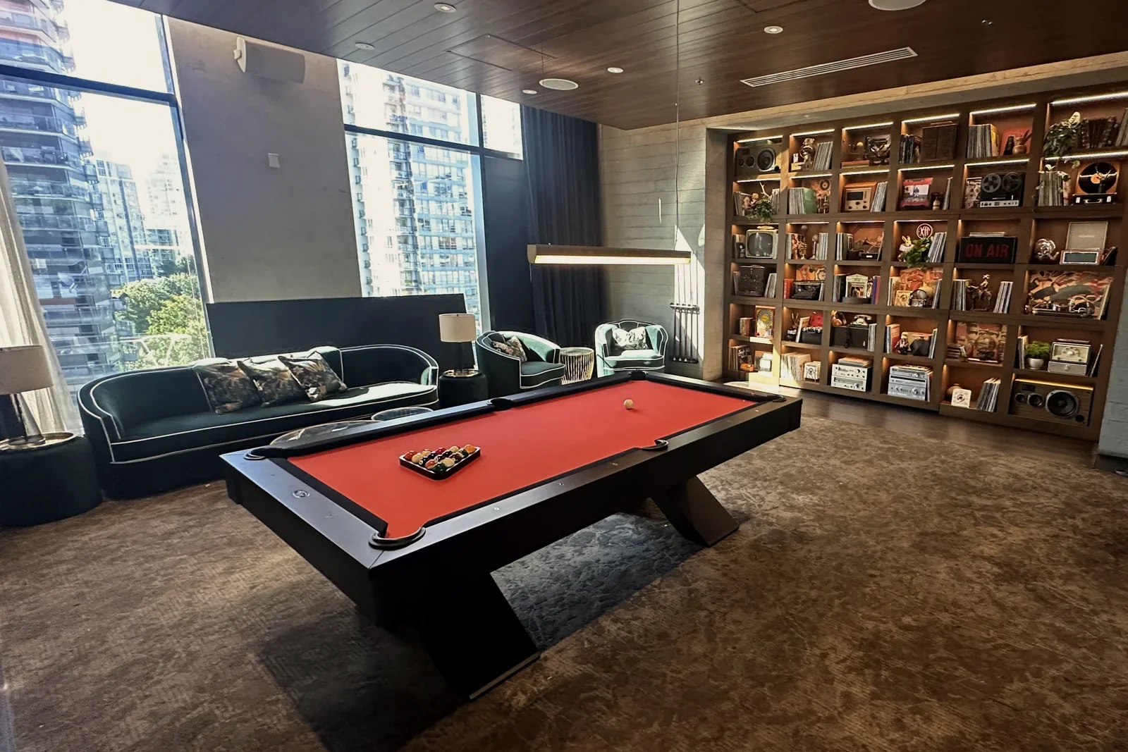 Wide view of a red-cloth pool table, green lounge seating and illuminated shelving in a film-production setting