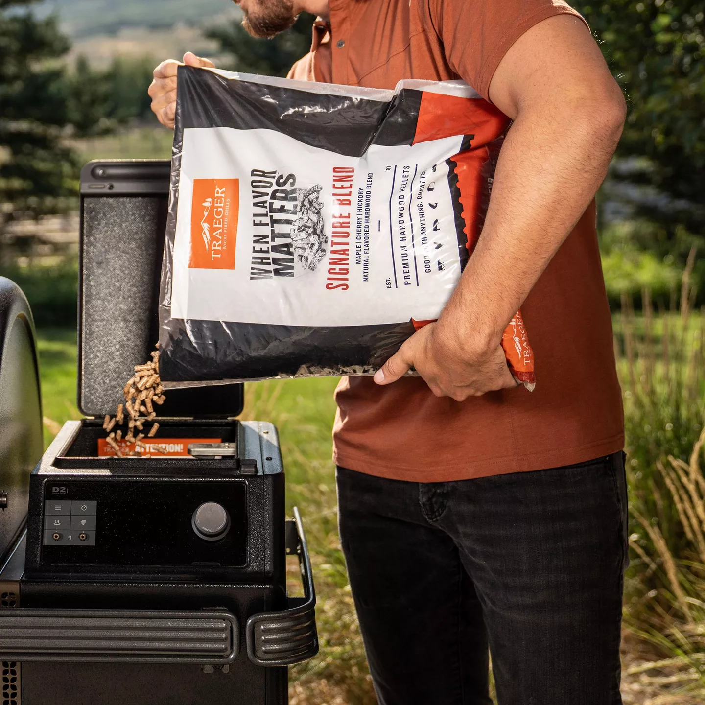 Person pouring a Signature Blend pellet bag into a Traeger hopper outdoors; strongest direct-use pellet image found.