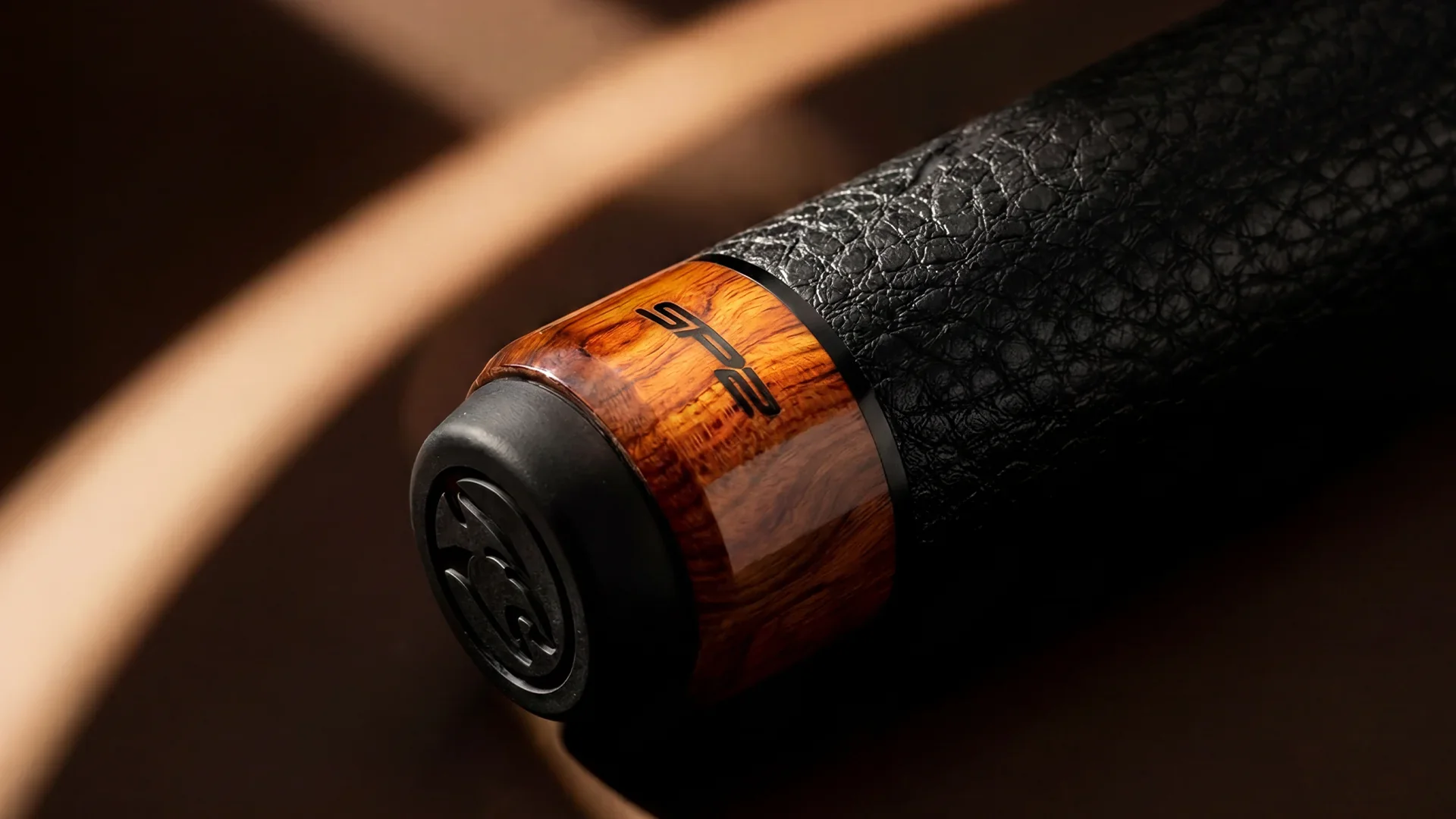 Close-up of a pool cue with warm wood grain and a textured black grip