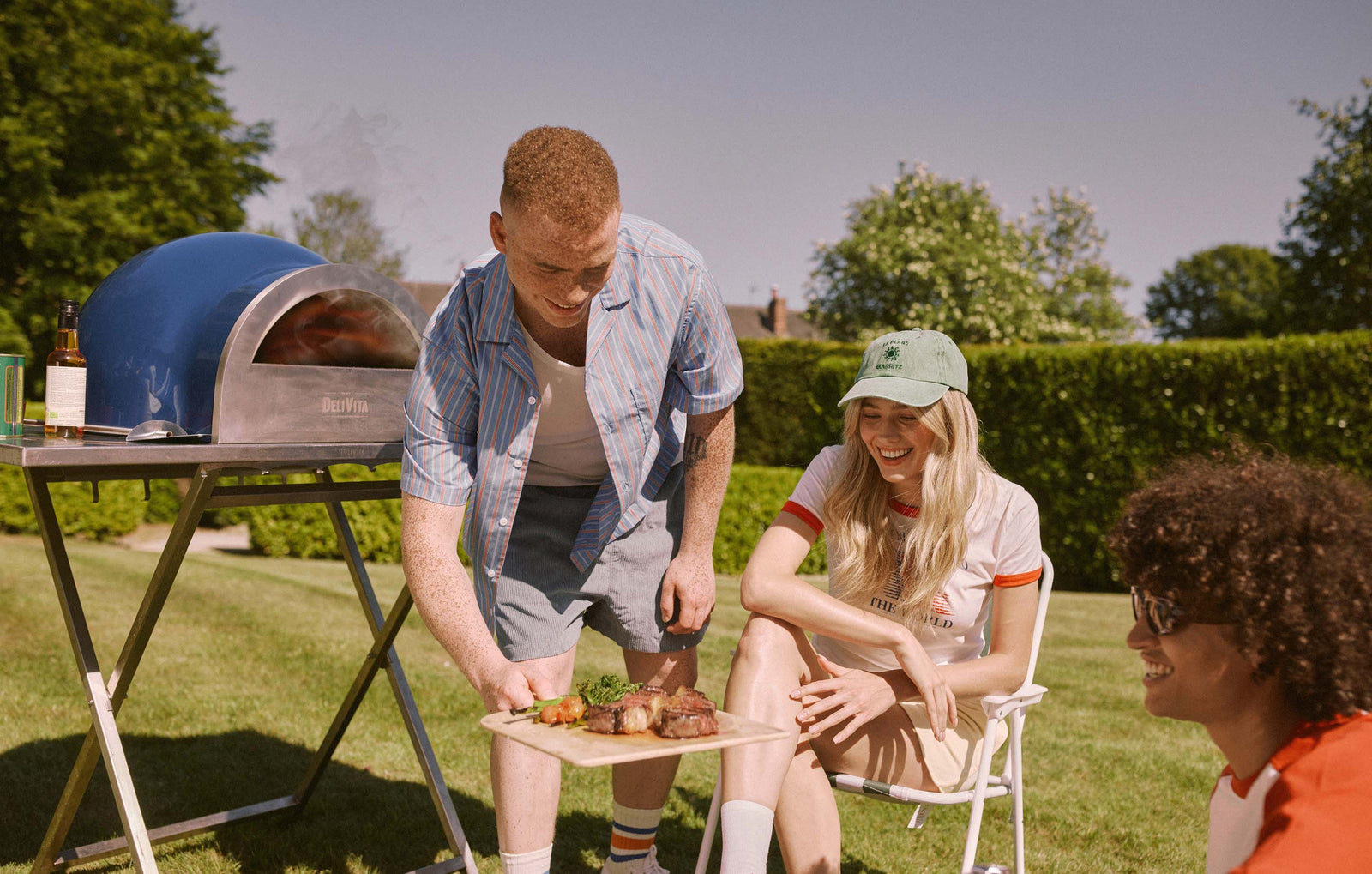 Friends sharing food in a garden beside a blue DeliVita oven