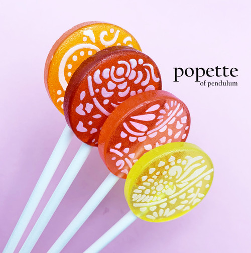 Four round, glossy hard candy lollipops on top of extra long white paper lollipop sticks. Shown upright in a row, from the bottom up, our bright yellow Lemonade lollipop with flower petals and white frosting,  our Strawberry Cream with flower petals and white frosting, our deep red Raspberry lollipop with flowers and white frosting and on the top part of the photo is our bright orange Mango lollipop with flowers, swirls and white frosting.  All on a light pink/purple background.