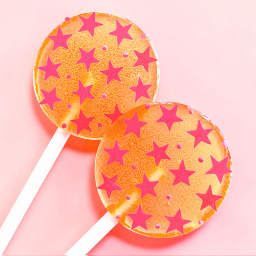 Two bright orange, round, smooth, glossy hard candy Tropical Punch Lollipops with extra long white paper lollipop sticks, each with coral pink color flavor star pattern on a light coral pink background.