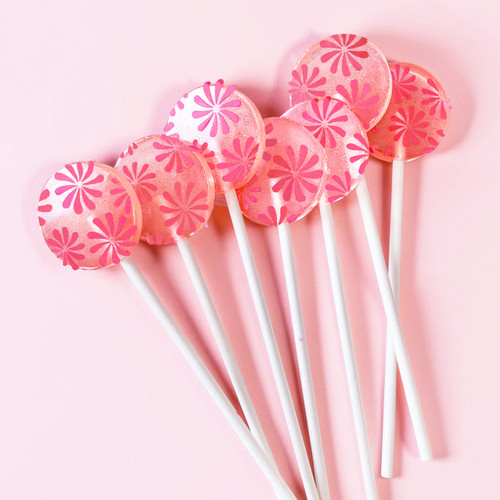 Seven light pink, round, glossy Strawberry Banana hard candy Lollipops with extra long white paper lollipop sticks and coral pink color pinwheel flavor flowers, on a light pink background showing very pink-on-pink flower bunch arrangement.