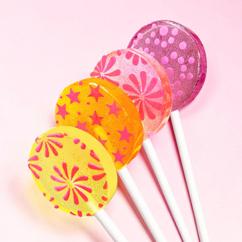 Four smooth, round, glossy hard candy lollipops on top of an extra long white paper lollipop stick. Shown upright in a row, our bright yellow Banana Cream lollipop with coral pink color pinwheel flavor flowers. Our bright orange Tropical Punch with coral pink color flavor stars. Our light pink Strawberry Banana with coral pink pinwheel flavor flowers and on the top part of the photo is our light purple Berries and Cream with round spiral confetti-like flavor dots, all on a light pink background.