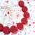 A collection of several red lollipops with blue dot patterns on white sticks. The lollipops are scattered on a white surface with pink, red, and blue confetti.