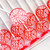 Several light coral pink round, glossy lollipops with white flower petal motifs on lollipop sticks on top of parchment paper on a bakers tray.
