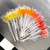 Multi, bright and colorful round, glossy hard candy lollipops on top of extra long white paper lollipop sticks in clear bags on a stainless steel table, in a fan shape. Bright yellow, orange, coral pink and red.
