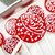 Several smooth, round, glossy deep bright red hard candy lollipops on top of extra long white paper lollipop sticks with white flower designs. All on a candy production tray.