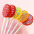 Five colorful lollipops on long white paper sticks are arranged against a light pink background in a fan layout. The lollipops are red, yellow, and orange, each with a pattern of dots in a contrasting color.