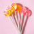 Six bright colored, round, smooth, glossy hard candy Lollipops with extra long white paper lollipop sticks, each with coral pink decorative pattern on a light pink background.