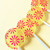 Four bright yellow, round, glossy hard candy Banana Cream Lollipops with extra long white paper lollipop sticks, each with coral pink color pinwheel flavor flowers on a light butter yellow color background.