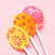 Three bright colored, round, smooth, glossy hard candy Lollipops with extra long white paper lollipop sticks, each with coral pink color flower pattern on a light pink background.