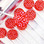 Nine coral pink lollipops on white paper sticks arranged on a bakery tray, showing detail of light pink dot pattern on each lollipop.