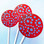 Three bright deep red round, smooth, glossy hard candy lollipops with extra long white paper lollipop sticks, each with blue polka dot frosting pattern on a light blue background.