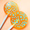 Two bright orange round, smooth, glossy hard candy lollipops with extra long white paper lollipop sticks, each with blue polka dot frosting pattern on a light peach background.