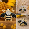gold and black bee snap jewelry charm with clear rhinestones on the thorax and black rhinestone eyes, shown loose and set in a round gold pendant with honeycomb background