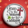 Round SnapAccents snap jewelry charm with "Jesus is the reason for the season" text, featuring a red and black buffalo plaid cross and green holly leaves, set against a festive red background with snowflake patterns.