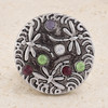 round snap jewelry charm with three silver dragonflies and six colorful rhinestones in purple, green, and clear on a textured gray background