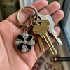 silver-tone snap jewelry keychain charm shaped like a flower with alternating black enamel and rhinestone petals held with keys in a hand