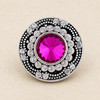 round snap jewelry charm with a faceted bright pink center stone surrounded by two rows of clear rhinestones on a silver-tone base with black detailing