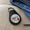 Black leather keychain with a round snap jewelry charm featuring the phrase It's The Most Wonderful Time Of The Year and a red and black plaid Christmas tree