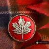 Red SnapAccents snap jewelry button featuring a detailed silver maple leaf design, perfect for fall and Canadian-themed accessories, displayed on a cozy plaid fabric background.