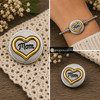 snap jewelry charm with a golden heart surrounding the word Mom in black script on a brushed silver background, shown loose and installed on a silver bracelet