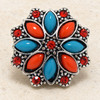 snap jewelry charm with a flower design featuring alternating dark coral and teal petal shapes surrounded by red rhinestones in a silver-tone setting