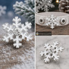 white enamel snowflake snap jewelry charm with a central clear rhinestone shown loose and attached to a light gray leather bracelet