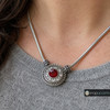 silver-tone snap jewelry necklace with a round pendant featuring a faceted red center rhinestone surrounded by clear rhinestones and decorative rope-like edging