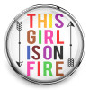 SnapAccents colorful snap jewelry charm with motivational phrase "This Girl Is On Fire" in bold multicolor letters, encased in clear round metal frame with black arrow designs, perfect for customizable snap bracelets or necklaces.