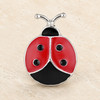 snap jewelry charm shaped like a ladybug with red enamel wings, black spots, and silver metal outline on a beige surface