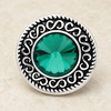 round snap jewelry charm with a large faceted green gem center and intricate silver scrollwork border