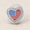 Round snap jewelry charm with a heart-shaped American flag design in red, white, and blue, surrounded by clear rhinestones on a silver base