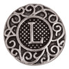 Round silver SnapAccents snap jewelry charm with intricate scrollwork design and raised letter "L" in the center on a textured black background, perfect for personalized interchangeable bracelets and accessories.